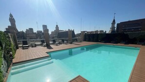 A rooftop swimming pool with wooden deck and lounge chairs, surrounded by city buildings and clear skies. - Fantastic Studio With Balcony Pool (Buenos Aires)