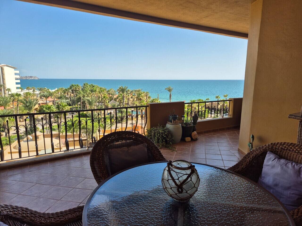 Un balcon avec vue sur l’océan, des meubles en osier et un objet décoratif en verre posé sur la table.