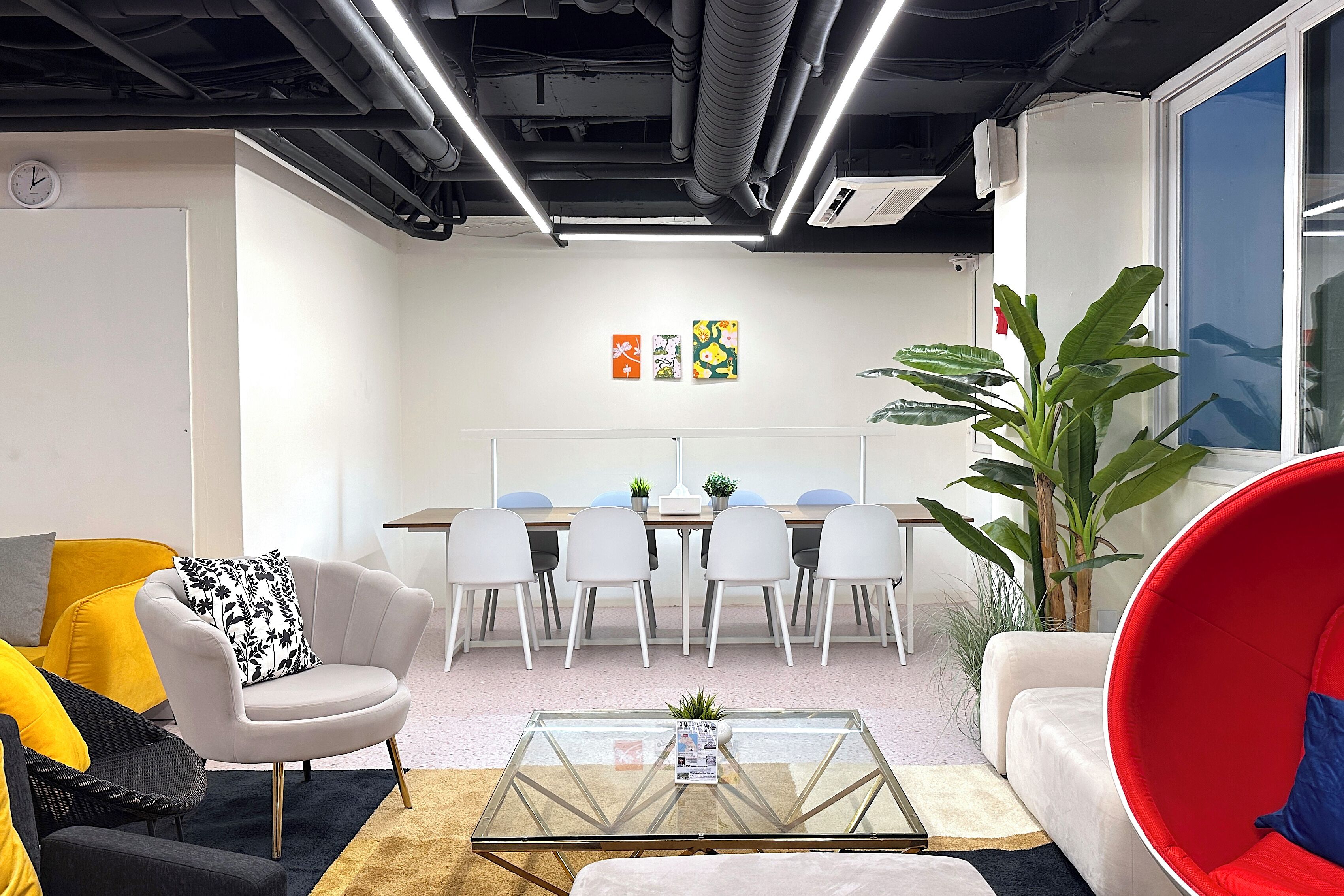 Un espacio de oficina moderno con una mesa de reuniones, sillas blancas, una mesa baja de vidrio y una silla roja.