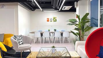 Un espacio de oficina moderno con una mesa de reuniones, sillas blancas, una mesa baja de vidrio y una silla roja.