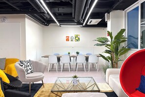 Un espacio de oficina moderno con una mesa de reuniones, sillas blancas, una mesa baja de vidrio y una silla roja.