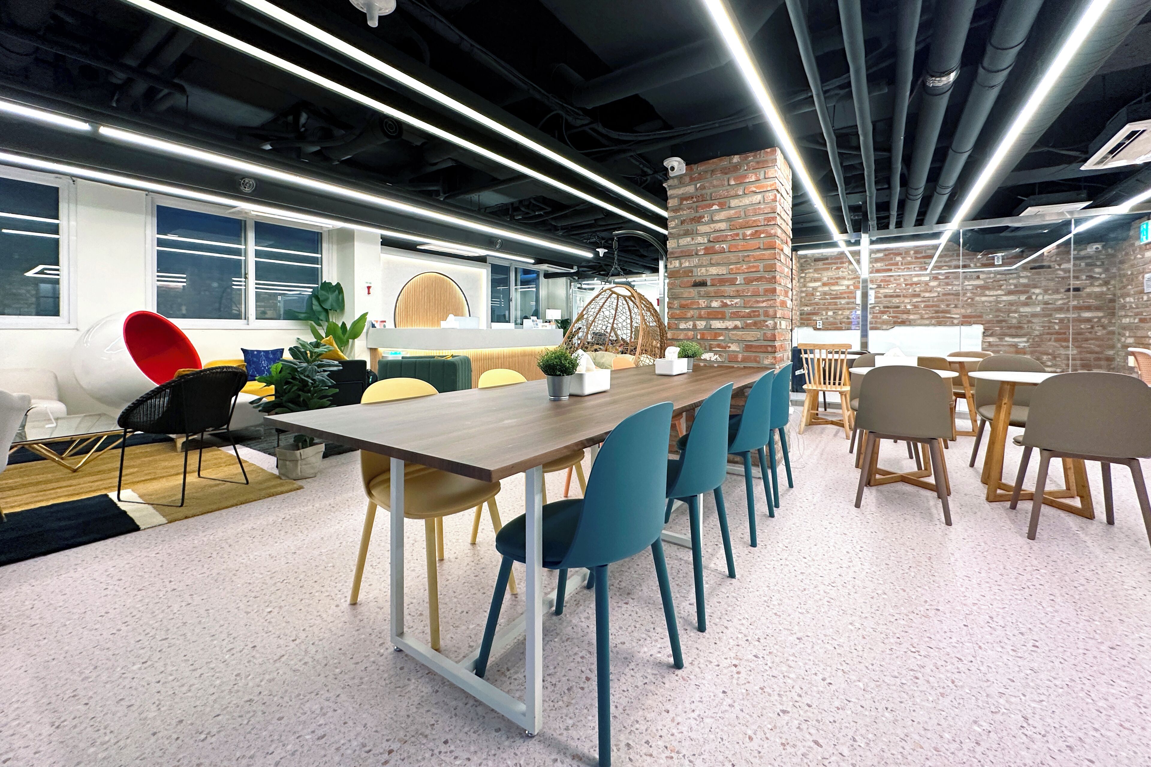 A modern office space with a long wooden table, blue chairs, and a brick accent wall.