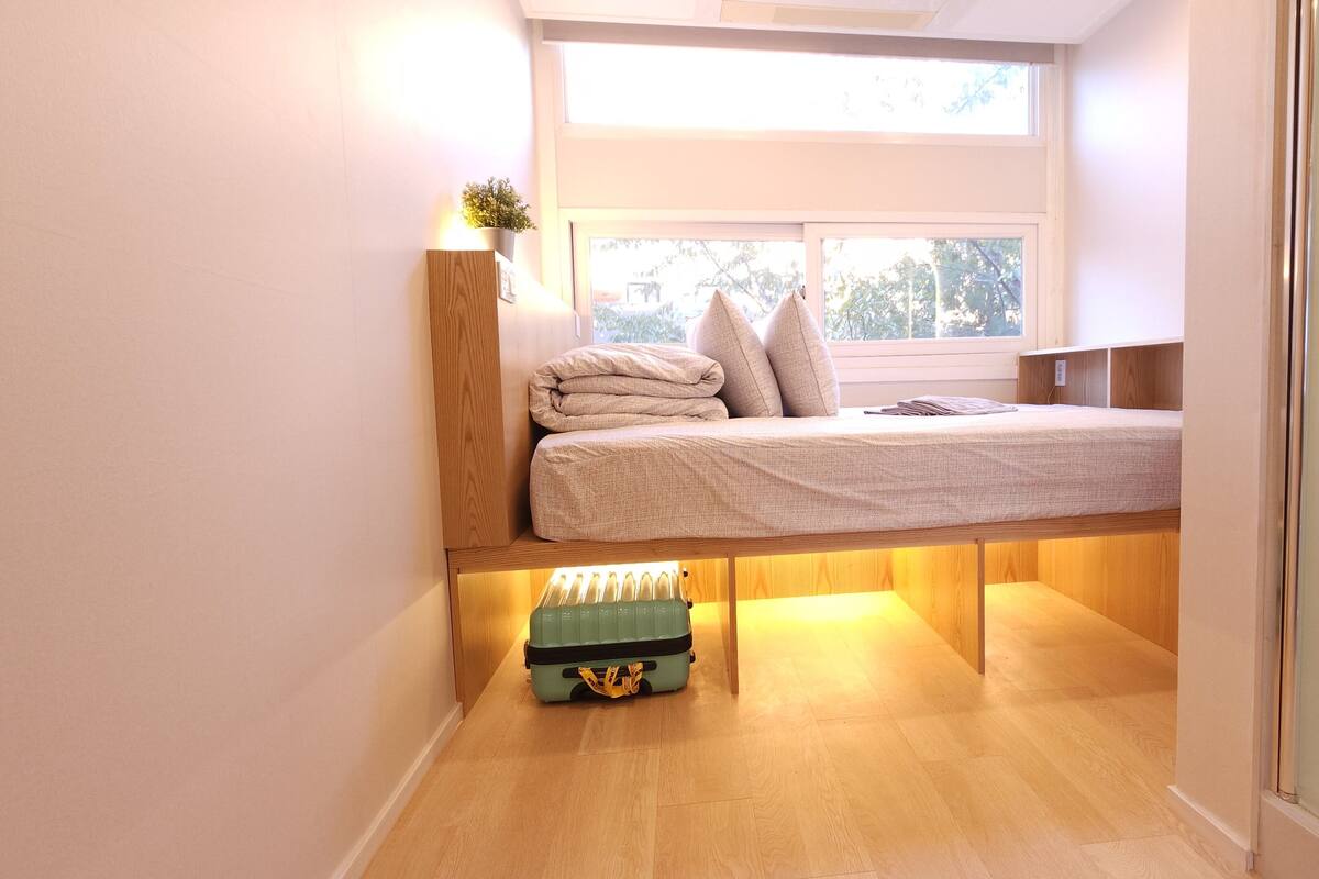 Een kleine slaapkamer met een stapelbed, een klein raam en een nachtkastje met een lamp.