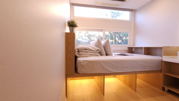 Een kleine kamer met een bed, een nachtkastje, een raam en een plant.