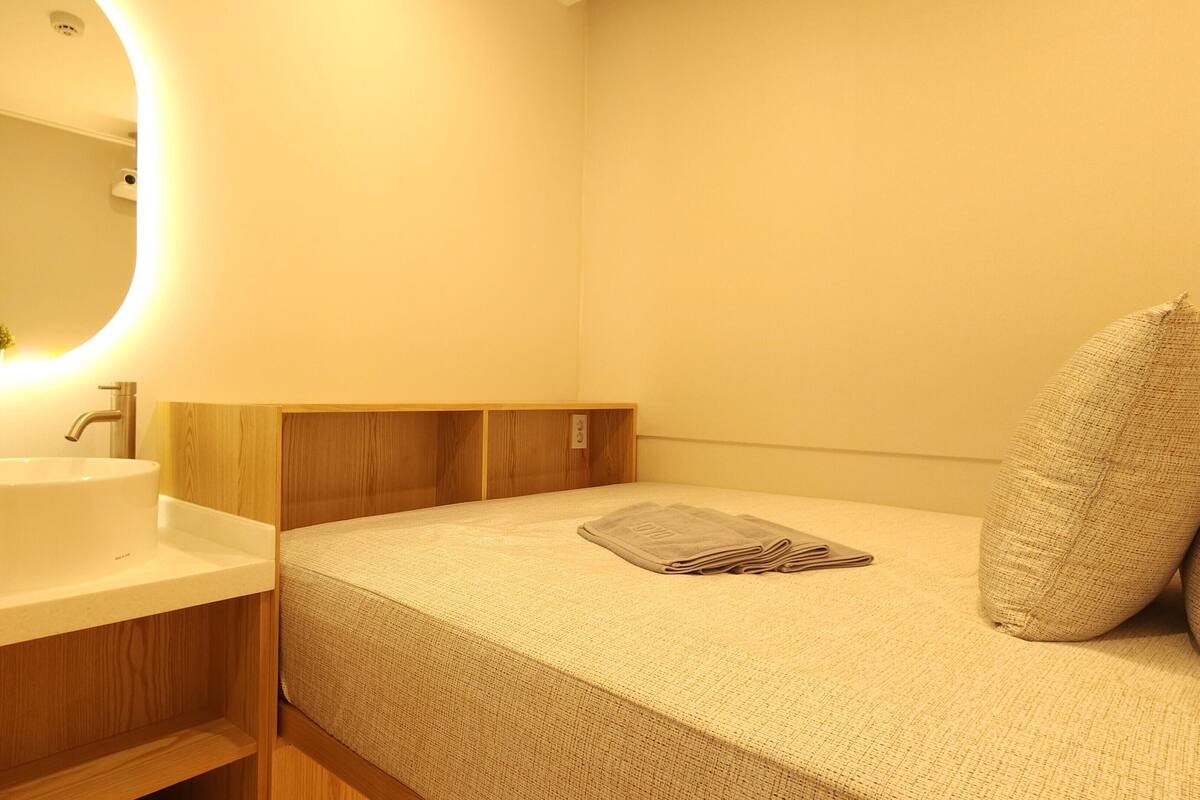 Een kleine, knusse slaapkamer met een enkel bed, een nachtkastje, een spiegel, en een badkamer met een wastafel en toilet.