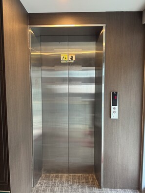 Een lift met een digitaal scherm, veiligheidsinstructies en een patroonloos tapijt.