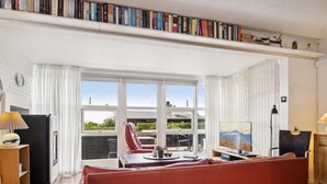 Una sala de estar moderna con un sofá rojo, un comedor con una mesa y sillas, un televisor y una estantería llena de libros.