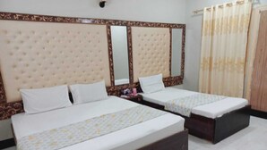 Een hotelkamer met twee enkele bedden, een groot gestoffeerd hoofdeinde, een spiegel en een gordijn.