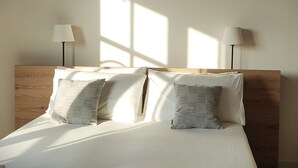 Un lit avec une literie blanche et deux oreillers, une tête de lit en bois et deux lampadaires placés de chaque côté.