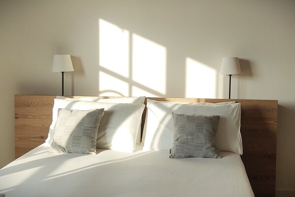A bed with white bedding and two pillows, a wooden headboard, and two floor lamps on either side.