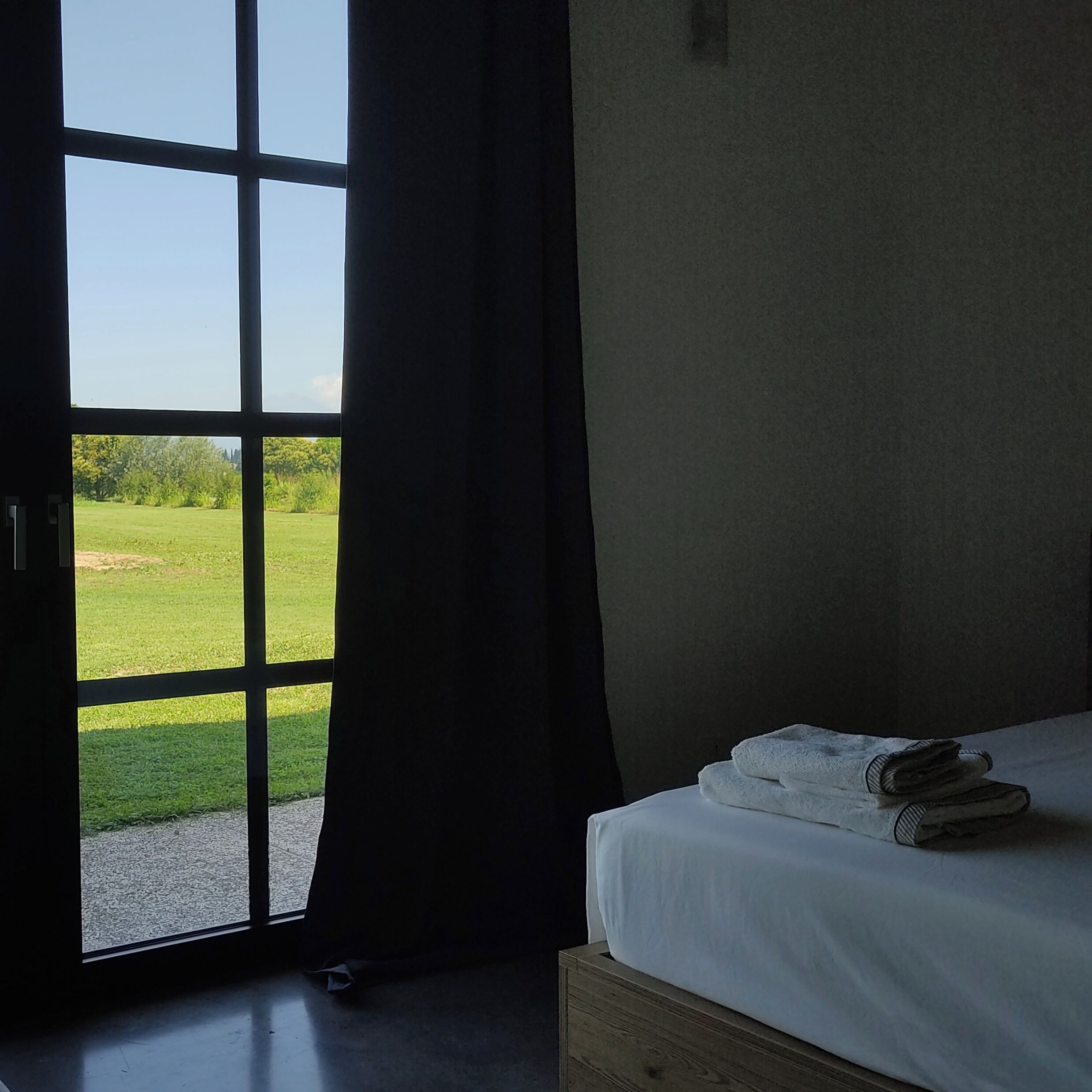 A hotel room with a large window, a bed with white linens, and a view of a green landscape.