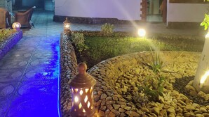 A nighttime outdoor area with a pathway, decorative lanterns, and a building with a white facade and arched windows.