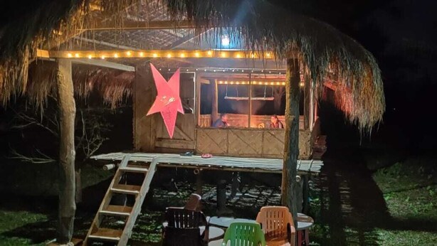 Una estructura con techo de paja, decorada con una estrella, y una mesa con sillas afuera, de noche.