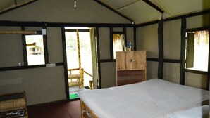 Una habitación con una cama individual, un armario de madera, una silla de mimbre y una ventana con vistas a zonas verdes.