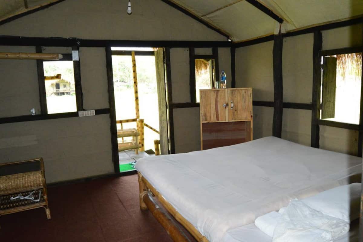 A room with a single bed, a wooden wardrobe, a wicker chair, and a window with a view of greenery.