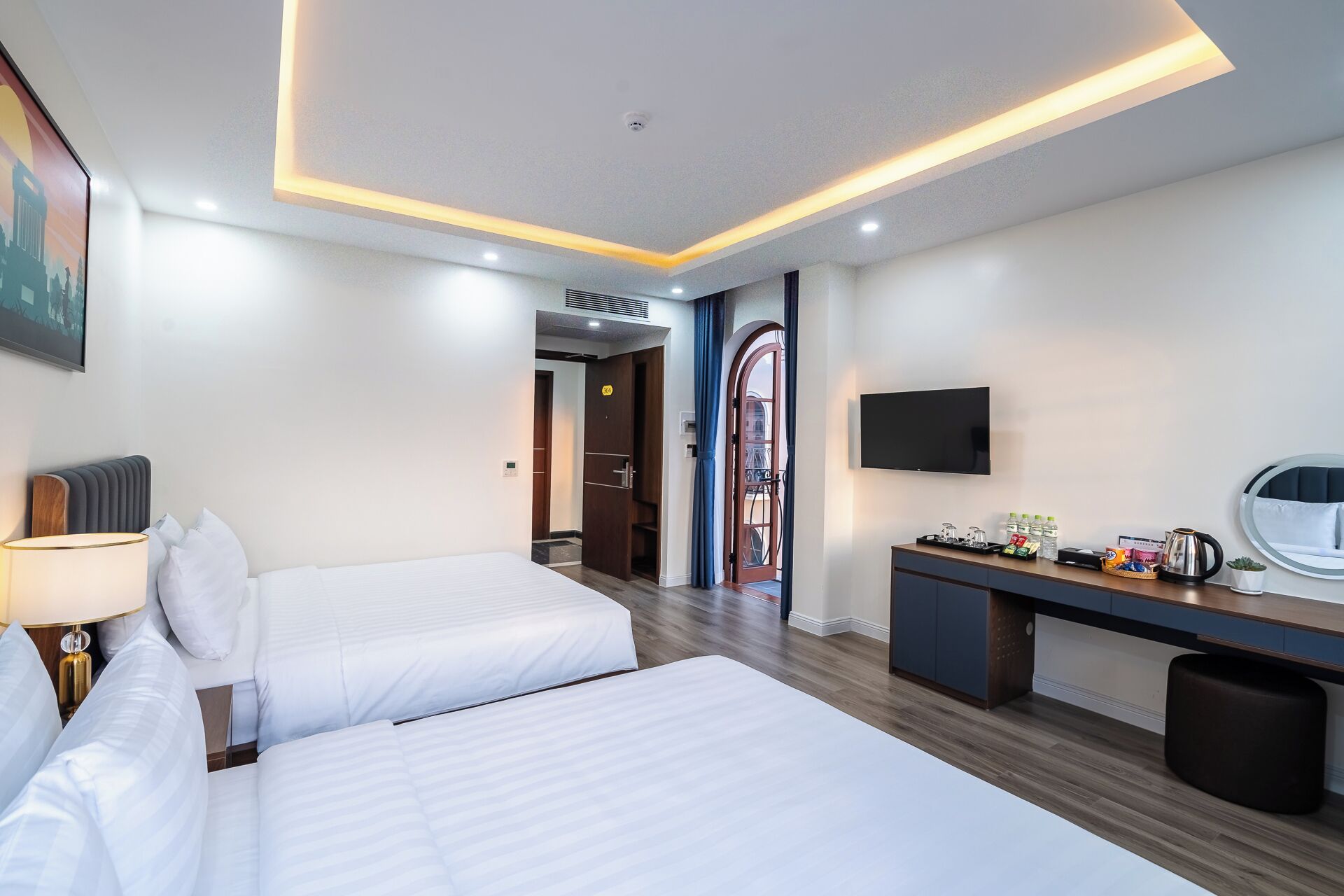 A hotel room with two beds, a desk with a flat-screen TV, a coffee maker, and a small trash bin.