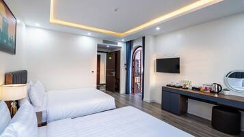 A hotel room with two beds, a desk with a flat-screen TV, a coffee maker, and a small trash bin.