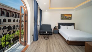 A hotel room with a bed, bedside table, and a view of a courtyard with a balcony. - Anston Castle Hotel (Phu Quoc)