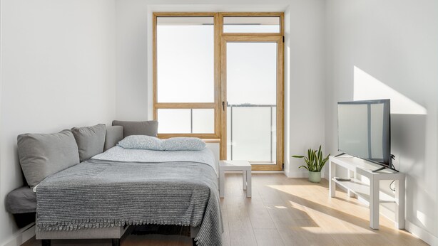 A modern bedroom with a bed, a TV stand, and a large window. - Cozy two room apartment near city center (Vilnius)