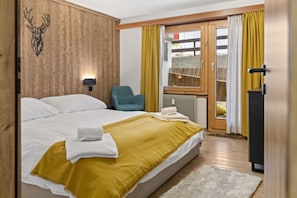 Ein Hotelzimmer mit einem großen Bett, einem hölzernen Kopfteil, einem blauen Sessel, einem Fenster mit gelben Vorhängen und Blick auf einen Zaun.