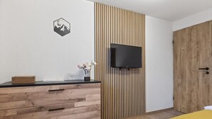 A bedroom with a wooden dresser, a TV mounted on a slatted wall, a bed with a yellow blanket, and a wooden door. - Saas-Fee center - 2 bedrooms - balcony and patio (Saas-Fee)