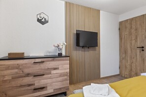 A bedroom with a wooden dresser, a TV mounted on a slatted wall, a bed with a yellow blanket, and a wooden door. - Saas-Fee center - 2 bedrooms - balcony and patio (Saas-Fee)
