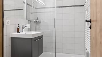 Ein modernes Badezimmer mit Duschkabine aus Glas, einem weißen Waschbecken inklusive Spiegel und einem Handtuchhalter.