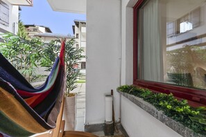 A balcony with a hammock, a window with a view of neighboring buildings, and a planter box with greenery. - Saas-Fee center - 2 bedrooms - balcony and patio (Saas-Fee)