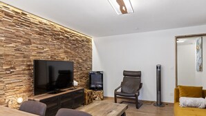 A modern living room with a stone wall, a flat-screen TV, a wooden coffee table, a brown leather chair, and a yellow sofa. - Saas-Fee center - 2 bedrooms - balcony and patio (Saas-Fee)