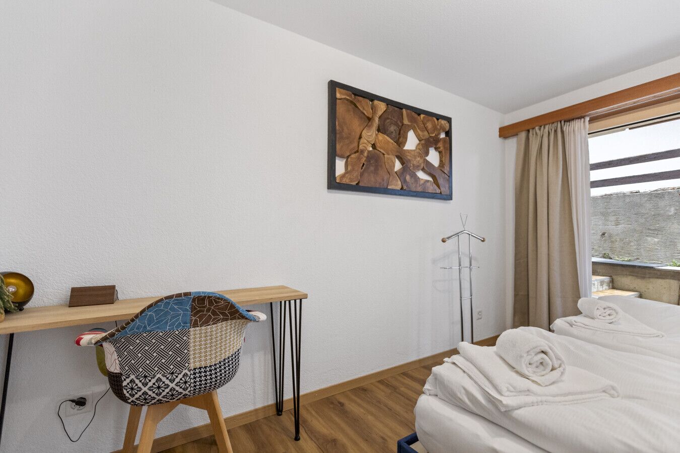 Ein Hotelzimmer mit einem Bett, einem kleinen Schreibtisch mit Stuhl, einem Kleiderständer und einem Fenster mit Vorhängen.