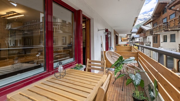 A wooden deck with a table and chairs, large windows, and a view of a mountain. - Saas-Fee center - 2 bedrooms - balcony and patio (Saas-Fee)