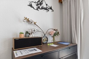 A desk with a Thomson speaker, two potted plants, a vase with flowers, and a decorative wall piece. - Saas-Fee center - 2 bedrooms - balcony and patio (Saas-Fee)