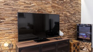 A modern living room with a large flat-screen TV mounted on a wooden wall with a stone-like texture. - Saas-Fee center - 2 bedrooms - balcony and patio (Saas-Fee)