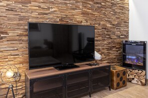 A modern living room with a large flat-screen TV mounted on a wooden wall with a stone-like texture. - Saas-Fee center - 2 bedrooms - balcony and patio (Saas-Fee)