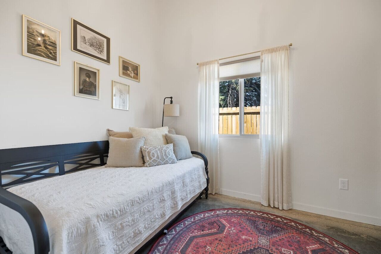 A bedroom with a bed, a window with curtains, and framed pictures on the wall.