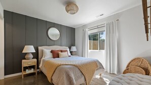 Un dormitorio con cama, mesitas de noche, un espejo y una ventana con cortinas.