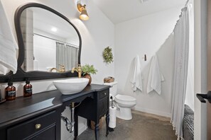 Ein Badezimmer mit großem Spiegel, weißem Waschbecken, schwarzem Waschtisch, Toilette und Duschvorhang.