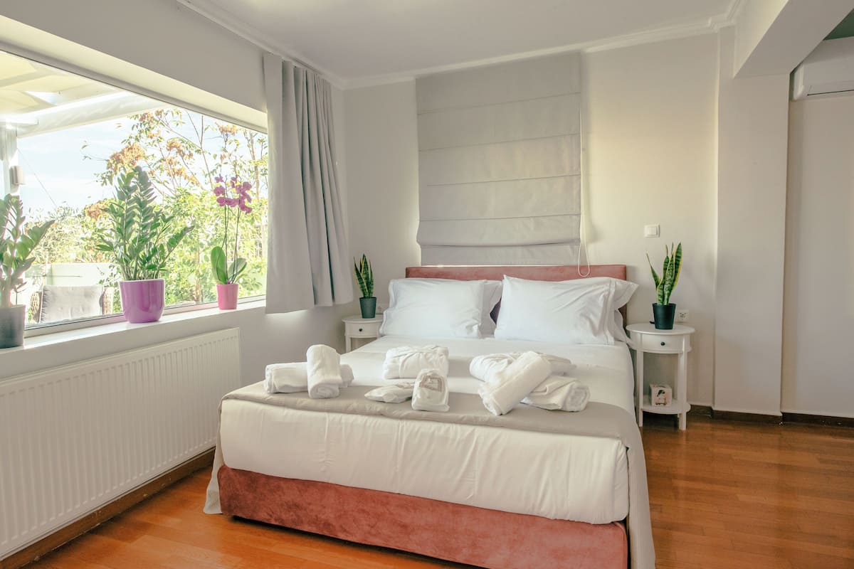 Une chambre moderne avec un grand lit, une fenêtre ornée de plantes et une vue sur la verdure environnante.