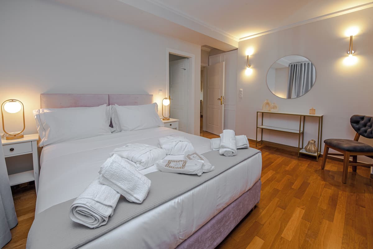 Un lit bien fait, agrémenté de serviettes pliées, une table de chevet avec une lampe, un miroir rond et une chaise dans une chambre d’hôtel moderne.