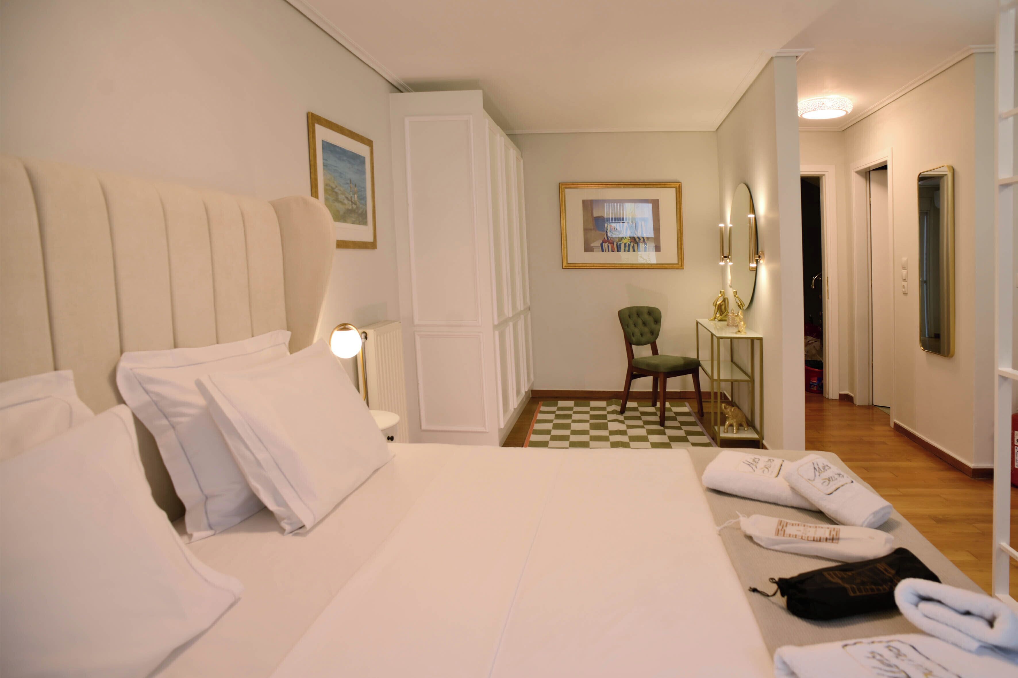 Et hotelværelse med en seng, puder, en stol, et bord med håndklæder, et indrammet billede og et spejl.