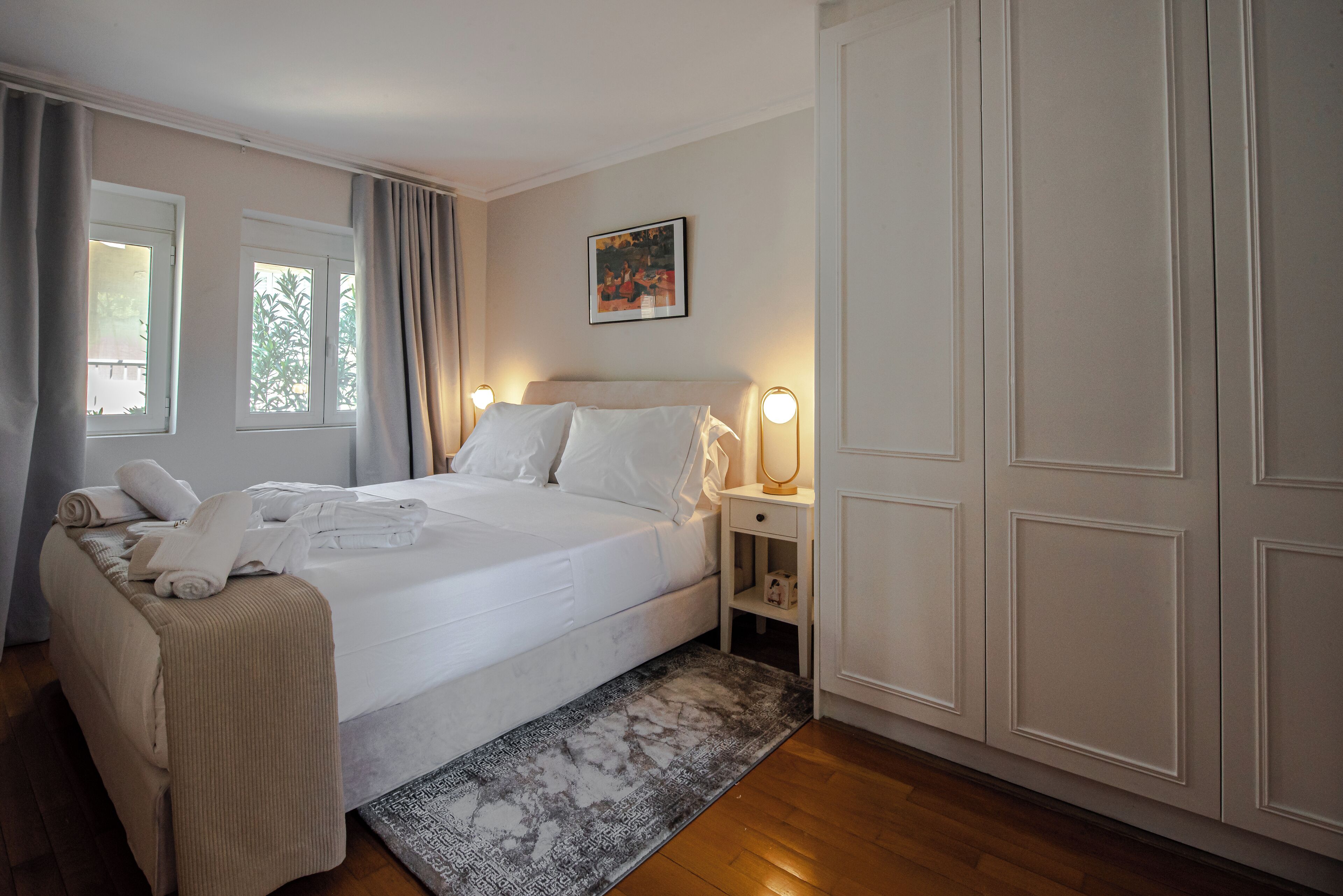 A neatly arranged bedroom with a bed, bedside tables, a nightstand, a wardrobe, and a window with curtains.