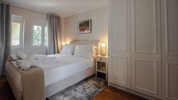A neatly arranged bedroom with a bed, bedside tables, a nightstand, a wardrobe, and a window with curtains.