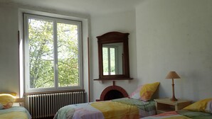 A bedroom with two beds, a window, a radiator, a mirror, and a bedside table with a lamp. - Beautiful, large family home (Nant)