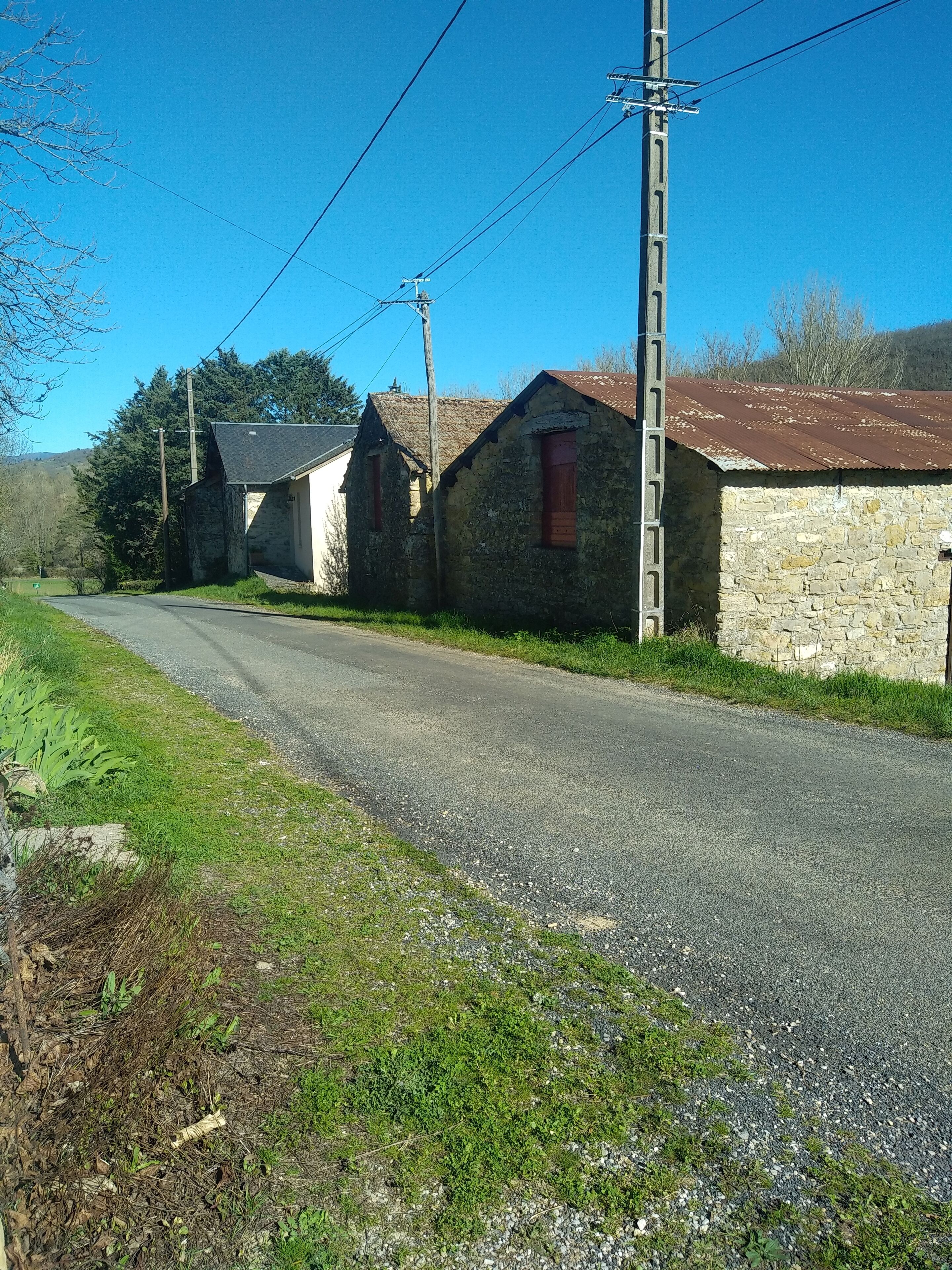 Una carretera rural con edificios de piedra, un poste de electricidad y un cielo azul despejado.