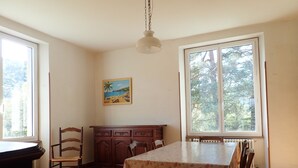 A dining area with a checkered floor, a table with a floral tablecloth, wooden chairs, a cabinet, and a painting of a beach scene. - Beautiful, large family home (Nant)