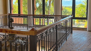 A balcony with wrought iron railings, a wooden floor, and large arched windows offering a view of greenery and mountains. - Palais Ako Atlas (Marrakech)