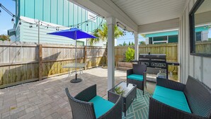 Un patio techado con muebles de mimbre, una parrilla y una sombrilla azul.