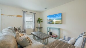 Una sala de estar con un sofá, una mesa de centro, un televisor montado en la pared y una ventana con cortinas.