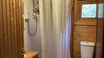 A wooden bathroom with a shower curtain, a toilet, and a window.