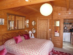 Interior de una cabaña de madera con una cama grande, zona de cocina y baño.